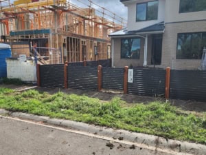 Transform your property with feature fence installation in Melbourne. Custom designs, expert craftsmanship, and durable materials tailored to your needs,Modern slat feature fence with timber posts in front of a newly constructed house and ongoing building work in the background.