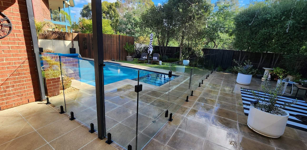 Glass pool fence surrounding a backyard pool.