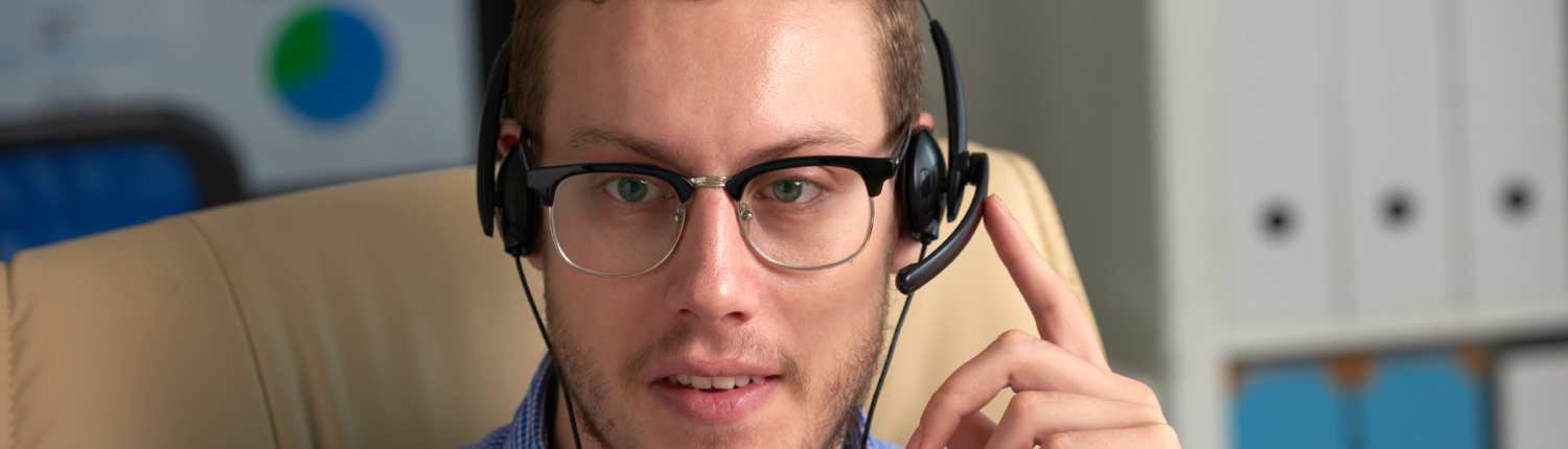 A male hotline operator wearing a headset, working at a desk in a call center environment with focused expression